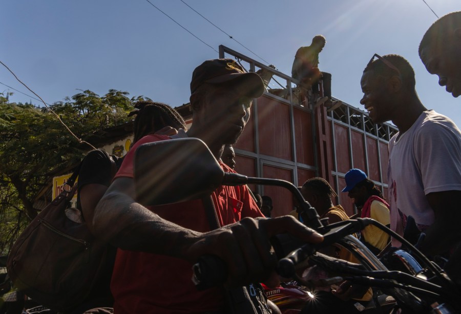 Neighbors pass in and out of a passageway as others erect a metal gate as protection against gangs, in the Petion-Ville neighborhood of Port-au-Prince, Haiti, Saturday, April 20, 2024. (AP Photo/Ramon Espinosa)