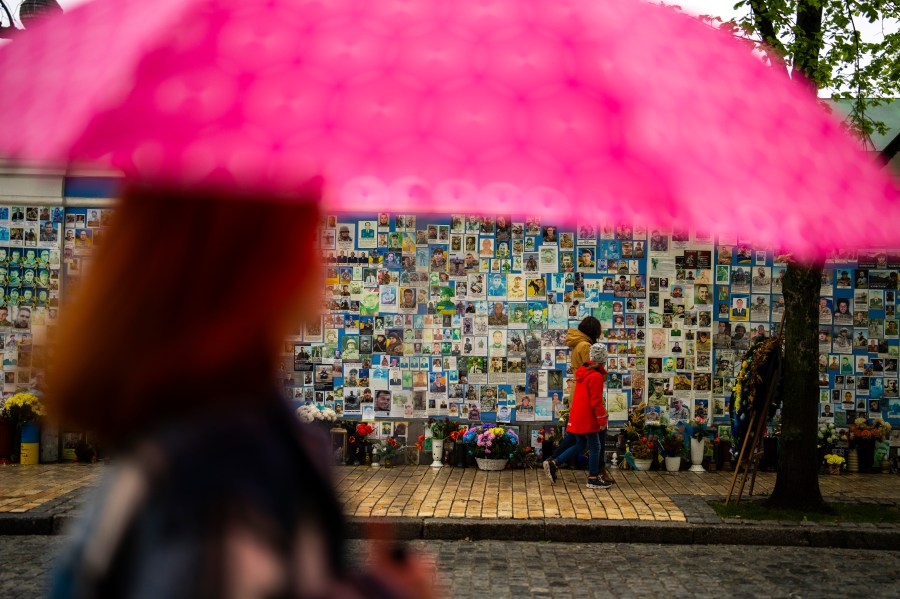 People walk past a memorial wall with photographs of Ukrainian soldiers killed during the war, at Saint Michael cathedral during a rainy morning in Kiev, Ukraine, Sunday, April 21, 2024. The House swiftly approved $95 billion in foreign aid for Ukraine, Israel and other U.S. allies in a rare Saturday session as Democrats and Republicans banded together after months of hard-right resistance over renewed American support for repelling Russia's invasion. (AP Photo/Francisco Seco)