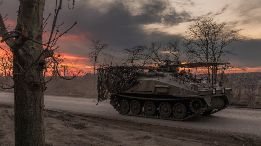 An armored personnel carrier is seen driving down a road against a dramatic sky.