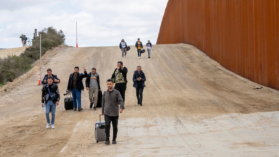 Migrants walk along the United States side of the border wall with Mexico to surrender to the U.S. Border Patrol near Campo, Calif.