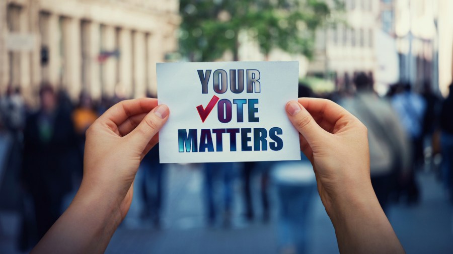 A person holds up a sign that reads "Your Vote Matters" in front of a blurred out crowd.