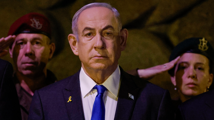 Israeli Prime Minister Benjamin Netanyahu stands as military personnel salute behind him.