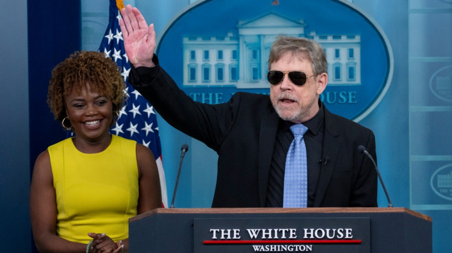 Actor Mark Hamill waves during a stop at a White House press briefing as press secretary Karine Jean-Pierre smiles off to the side.