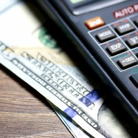 A $100 bill is visible sticking out from under a calculator in a close-up.