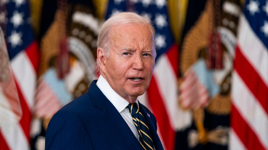 President Biden turns to speak in front of a line of American flags.