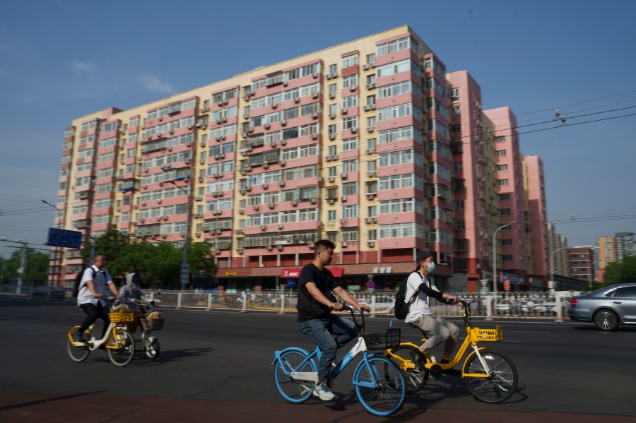 Chinese riding bicycle pass by a local business building the in background in Beijing, China, Friday, June 28, 2024. Surveys of Chinese factory managers showed a mixed outlook for the world's second-largest economy in June, with growth steady but not picking up much steam. (AP Photo/Vincent Thian)