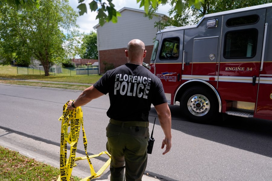 A member of the Florence, Ky., Police Department moves yellow police tape to allow an engine to pass into the area where a shooting took place, Saturday, July 6, 2024, in Florence, Ky. Police say several people were killed and others wounded in an early morning shooting during a party at this home in northern Kentucky. Police say the shooting suspect later died after fleeing the home and leading police on a vehicle pursuit that ended with the suspect's car falling into a ditch. (AP Photo/Carolyn Kaster)