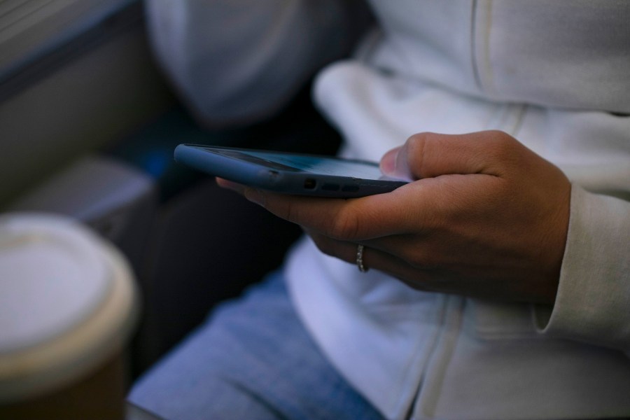 FILE - A woman looks at a hand held device on a train in New Jersey on May 18, 2021. (AP Photo/Jenny Kane, File)