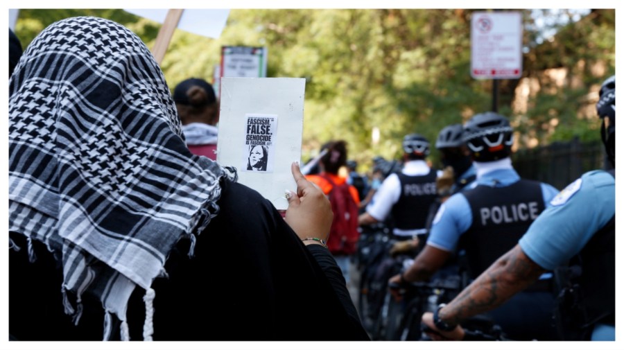 A pro-Palestinian protester at the March on DNC holds a small poster that includes an image of Democratic presidential nominee Kamala Harris with the words "Genocide is Fascism" on Monday, Aug. 19, 2024, in Chicago. (AP Photo/Martha Irvine)