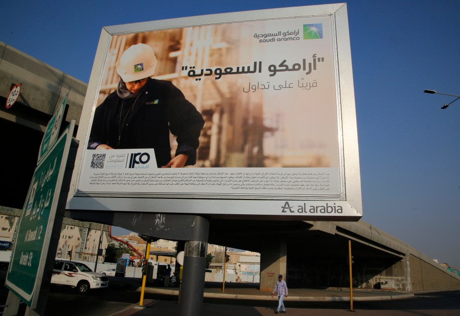 FILE - A man walks under a billboard displaying an advertisement for Saudi Arabia's state-owned oil giant Aramco with Arabic reading "Saudi Aramco, soon on stock exchange" in Jiddah, Saudi Arabia, on Nov. 12, 2019. (AP Photo/Amr Nabil, File)